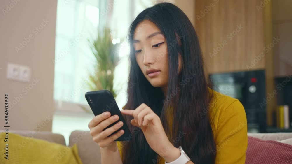 Attractive asian young woman use phone look around sitting on sofa at home. Social media text email enjoy distant communication. Social media. Close up. Slow motion Attractive asian young woman use phone look around sitting on sofa at home. Social media text email enjoy distant communication. Social media. Close up. Slow motion