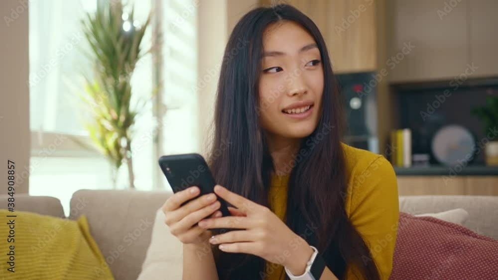 Happy asian young woman use phone sitting on sofa at home. Social media text email enjoy distant communication. Social media. Close up. Slow motion Happy asian young woman use phone sitting on sofa at home. Social media text email enjoy distant communication. Social media. Close up. Slow motion