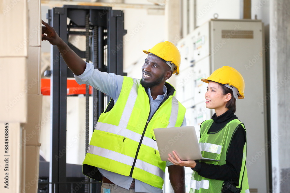 © Akarawut - African American and Asian workers wearing safety vest while working in warehouse checking for the inventory of product using laptop for industrial business