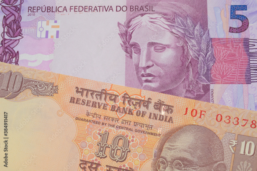 Fototapeta premium A macro image of a orange ten rupee bill from India paired up with a pink and purple five real bank note from Brazil. Shot close up in macro.