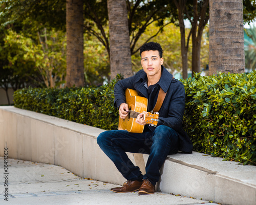 Young student sitting on the street in the city public park while playing guitar - street musician, student off-campus life, autumn break time photo