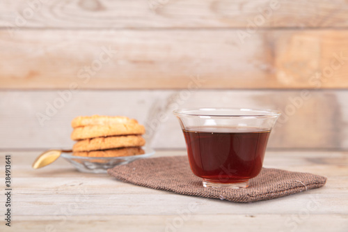 A bowl of hot black tea and a plate of refreshments on a wooden background