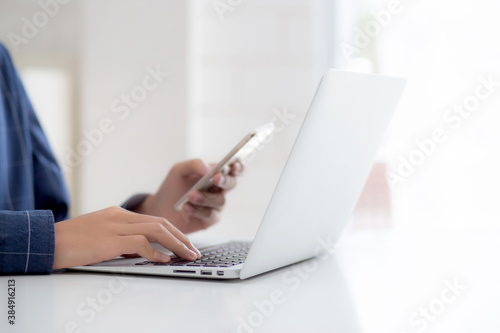 Closeup hand of young man working laptop computer and reading smartphone on internet online on desk at home, freelance male using phone with social media, business and communication concept.