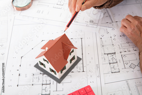 A hand holding a pencil pointing at the house model on the drawing