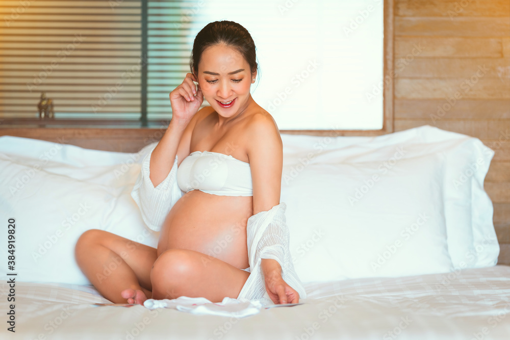A Beautiful woman Asian pregnant posing by hold picture baby In the stomach by sit on the bed her in happy emotional A Beautiful woman Asian pregnant posing by hold picture baby In the stomach by sit on the bed her in happy emotional
