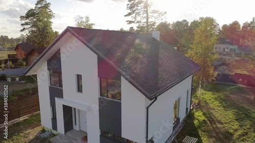 Aerial top view of new modern residential house cottage in a nice neighborhood. Roof made of soft tiles. A fence is being built around the house. Trees and lawn grow on the land
