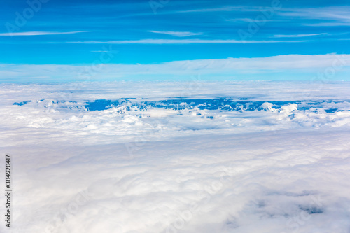 Aerial view above the clouds and misty mountain peaks covered with snow on a sunny day.China Tibet.