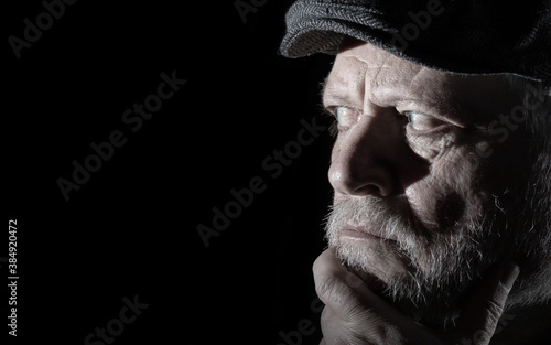 Portrait of an elderly man with a beard. He looks intently into the darkness. photo