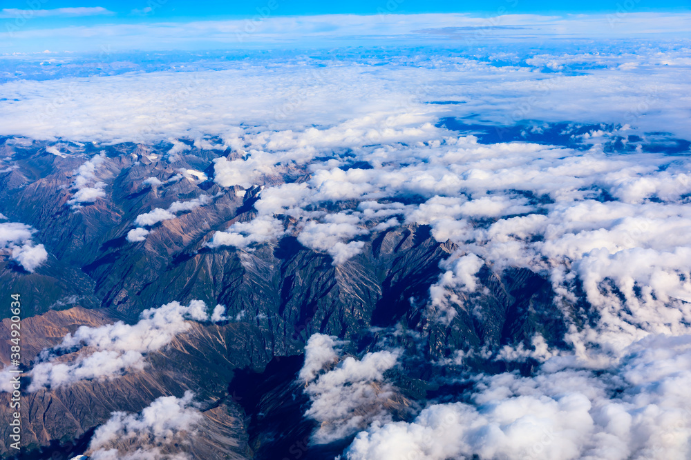 Aerial view above the clouds and mountain peaks on a sunny day.