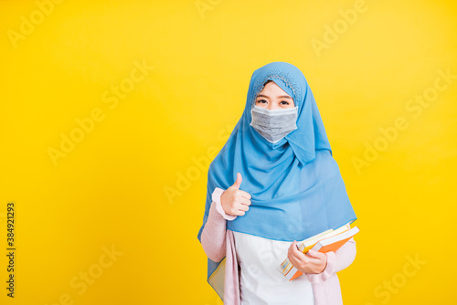 Asian Muslim Arab, Portrait of beautiful young woman religious wear veil hijab and face mask protective to prevent coronavirus hold books on hand and show finger thumb up for good sign Back to college © sorapop