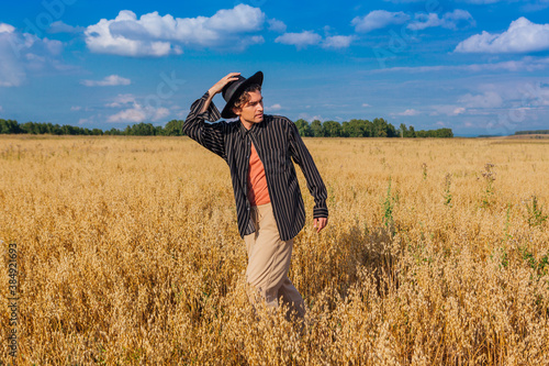 Tall handsome man with black hat standing at golden oat field.