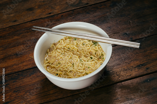 cooked instant noodle in white bowl with standless steel chopsticks on wooden table