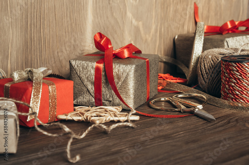 Christmas gift wrapping. Wrapped gifts, ribbons, decorations, scissors and paper on a wooden background. Copy space.