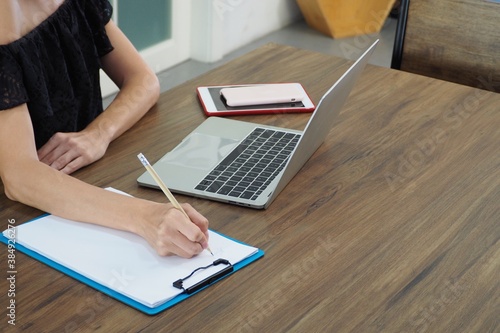 Young Caucasian woman working with computer and writing report on the paper Working from home and woman lifestyle concept