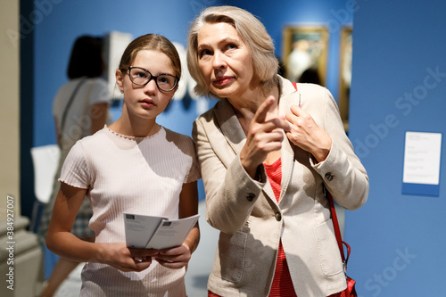 Intelligent female tutor helping tweenage girl exploring art pieces in art museum