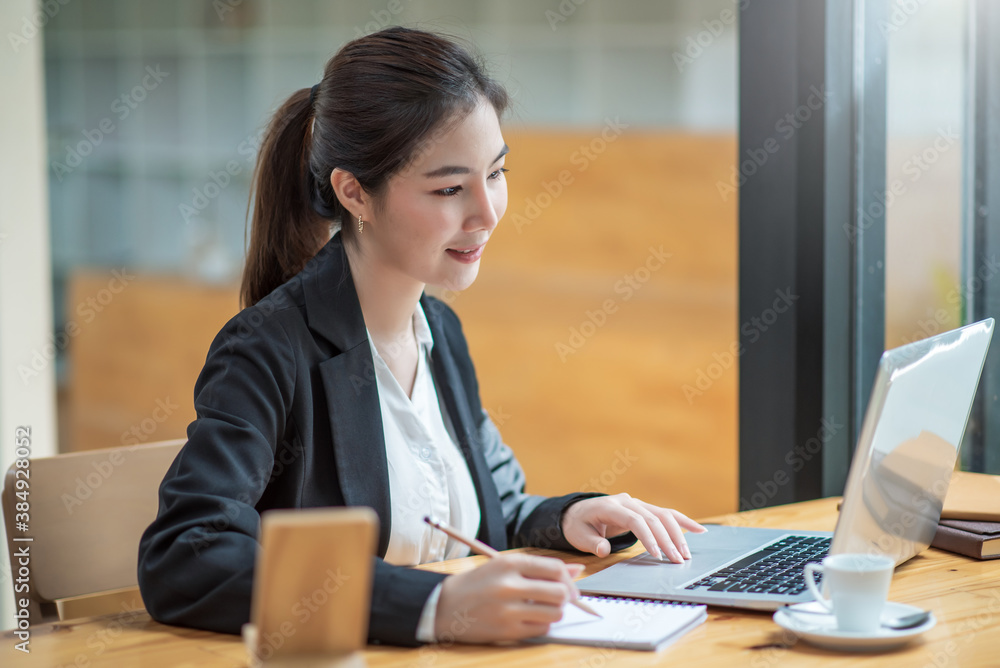 Charming asian businesswoman working on laptop and taking note while sitting at the table in office. Charming asian businesswoman working on laptop and taking note while sitting at the table in office.