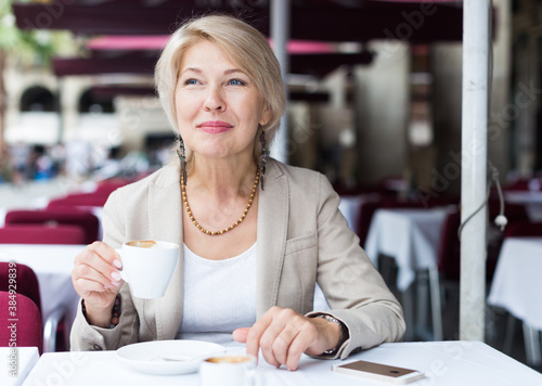 Mature businesswoman is drinking coffee in time breakfast in cafe. © JackF