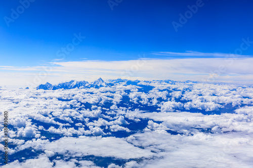 Aerial view above the clouds and misty mountain peaks covered with snow on a sunny day.China Tibet. © ABCDstock