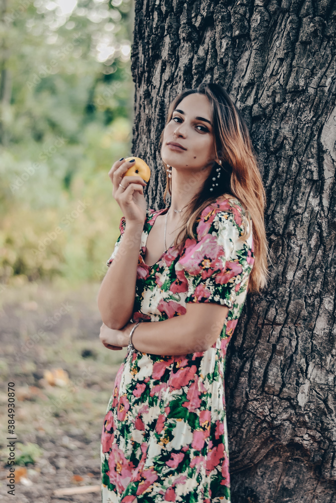 young beautiful girl in a multicolored sundress eating an apple in the forest young beautiful girl in a multicolored sundress eating an apple in the forest