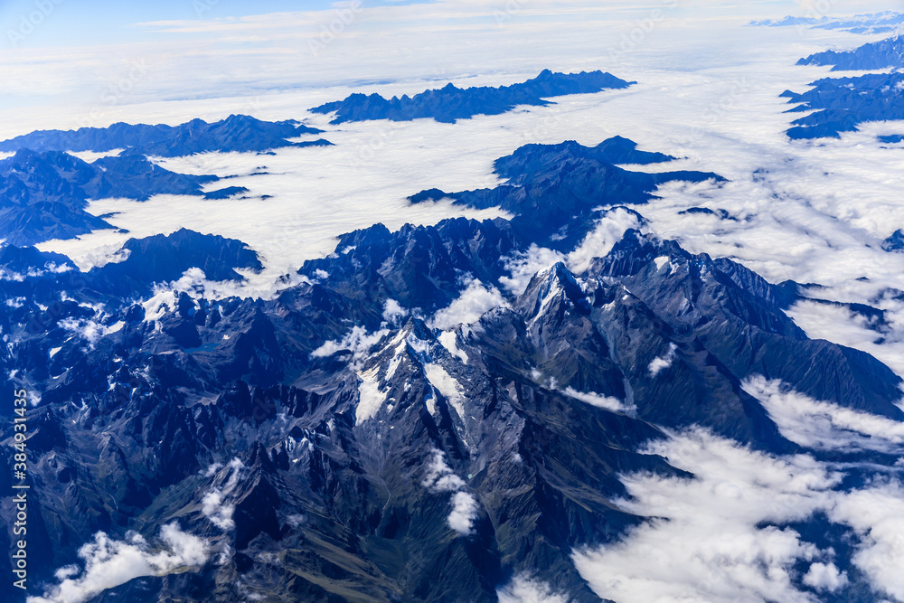 Fototapeta premium Aerial view above the clouds and mountain peaks on a sunny day.