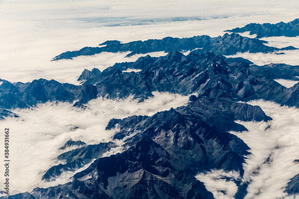 Aerial view above the clouds and mountain peaks on a sunny day.
