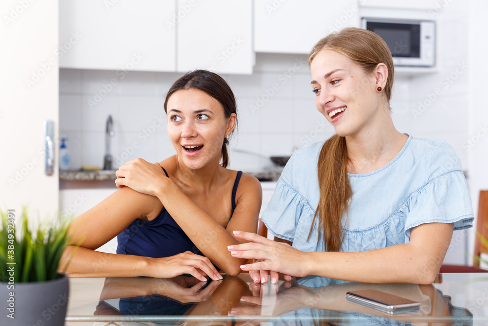 Fototapeta premium Portrait of two young women friends having expressional talking in kitchen interior