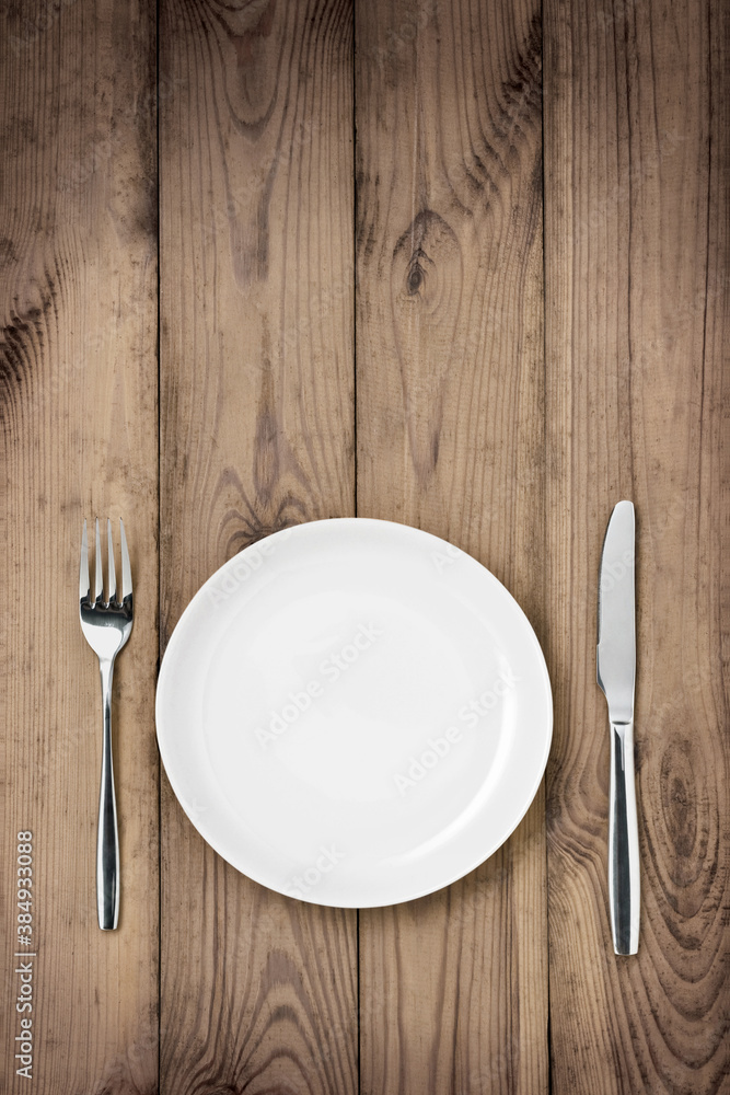 Empty white plate with knife and fork on a wooden table Empty white plate with knife and fork on a wooden table