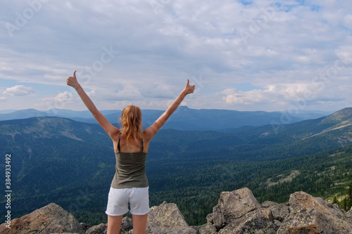A woman jumps, dances, and climbs, does yoga on top of mountains. Young woman hiking up hill against a blue sky with clouds.
