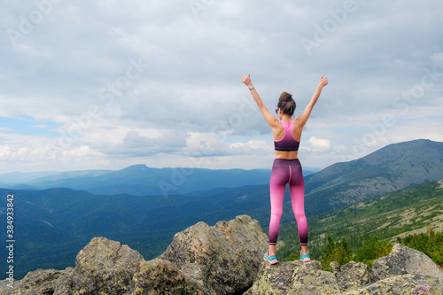Young woman hiking up hill against a blue sky with clouds. A woman jumps, dances, and climbs on top of mountains.