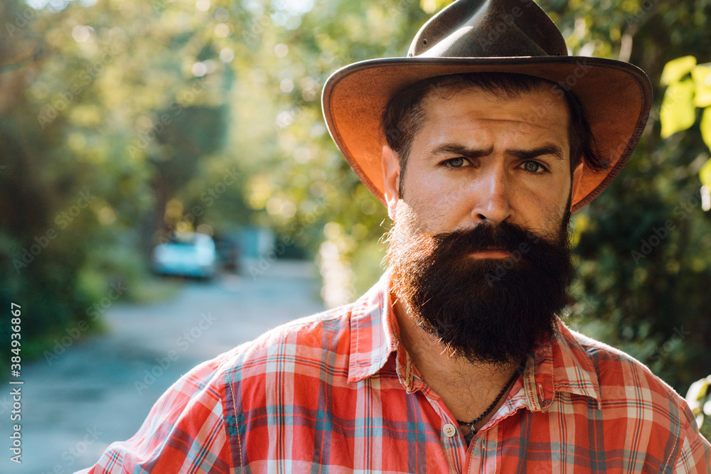Obraz premium Young handsome man in cowboy hat with long beard, mustache and trendy hairdo.