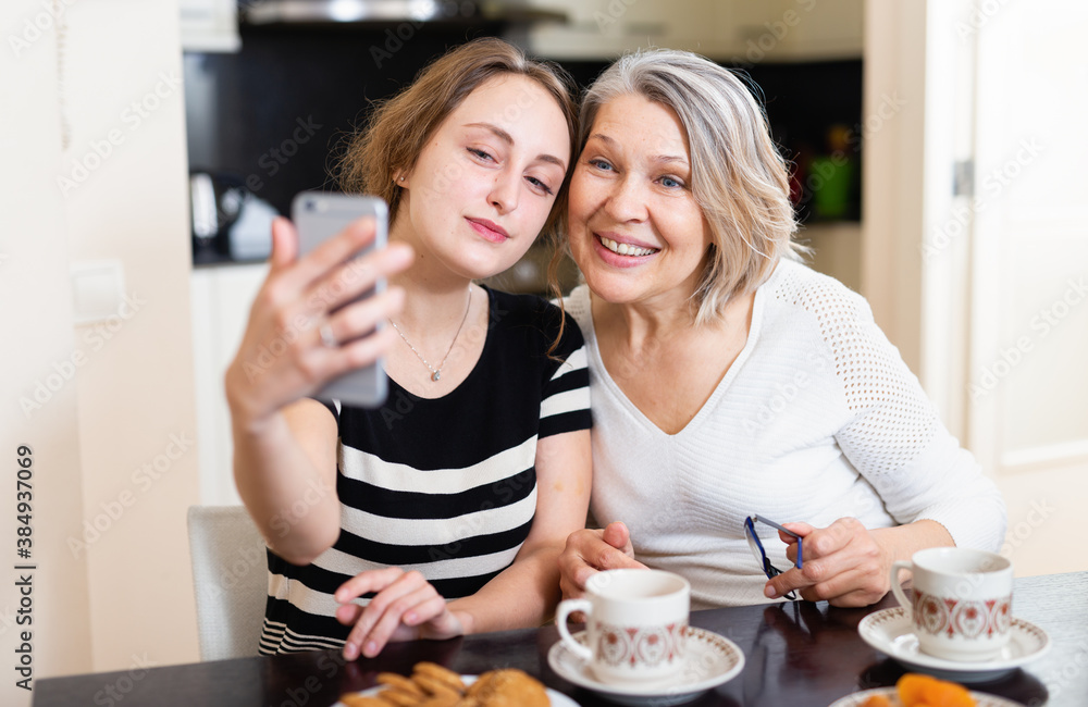Smiling young woman making selfie with elderly mother at home