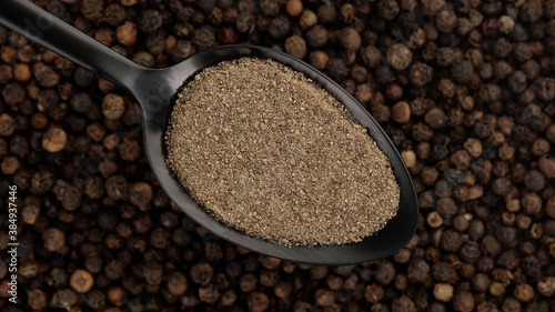 ground black pepper in spoon and  black peppercorns on background