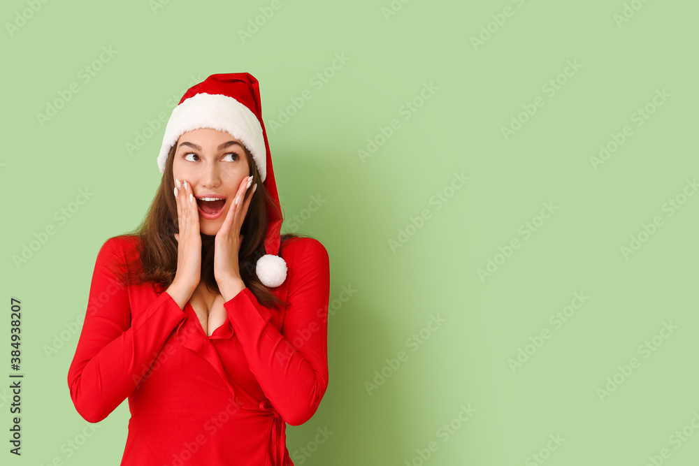 Surprised young woman in Santa hat on color background Surprised young woman in Santa hat on color background