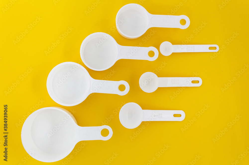 Set of white measuring cups, measuring spoons use in cooking lay on wooden yellow background in top view Set of white measuring cups, measuring spoons use in cooking lay on wooden yellow background in top view