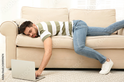 Lazy young man using laptop while lying on sofa at home photo