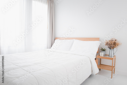 Beautiful white clean cozy bedroom interior with green and dried flowerpot on side wooden table