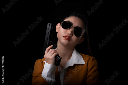 Portrait beautiful Asia woman wearing a yellow suit one hand holding a pistol gun at the black background photo