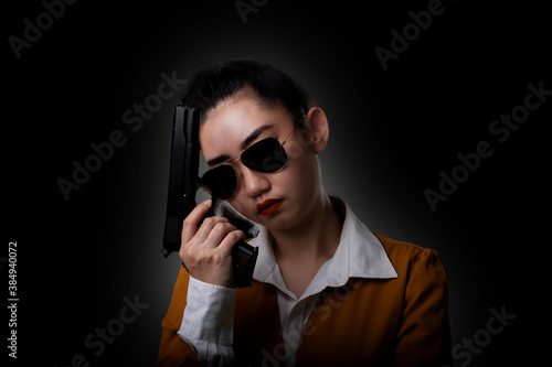 Portrait beautiful Asia woman wearing a yellow suit one hand holding a pistol gun at the black background photo