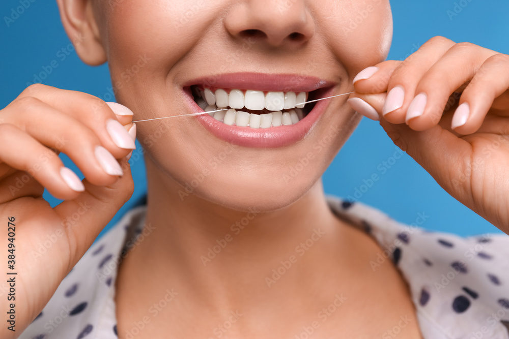 Young woman flossing her teeth on blue background, closeup. Cosmetic dentistry Young woman flossing her teeth on blue background, closeup. Cosmetic dentistry