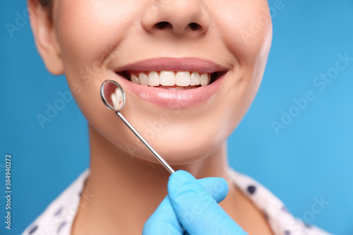 Doctor examining woman s teeth on blue background  closeup. Cosmetic dentistry