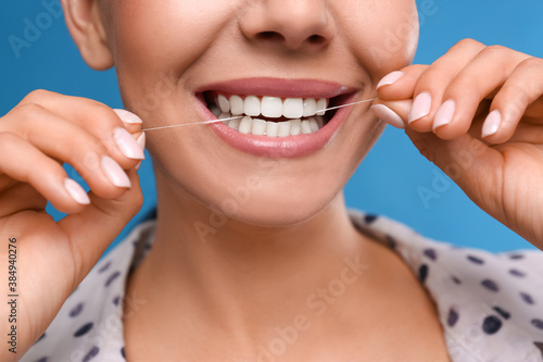 Young woman flossing her teeth on blue background  closeup. Cosmetic dentistry