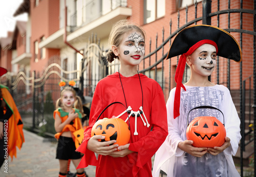 Cute little kids with pumpkin candy buckets wearing Halloween costumes going trick-or-treating outdoors