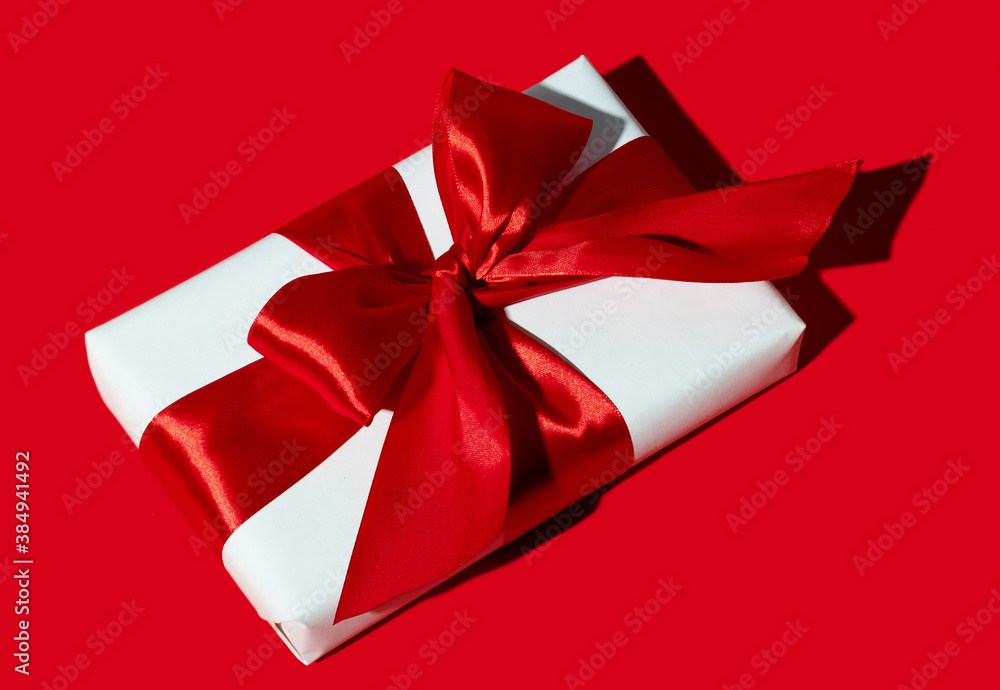 Holiday gift. Special occasion reward. Care package. Festive surprise. Present wrapped in white box with ribbon bow isolated on red background.