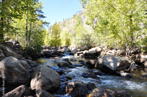 Pretty landscape scene of a flowing river with large rocks and boulders, with mountains and trees with fall colors in the background