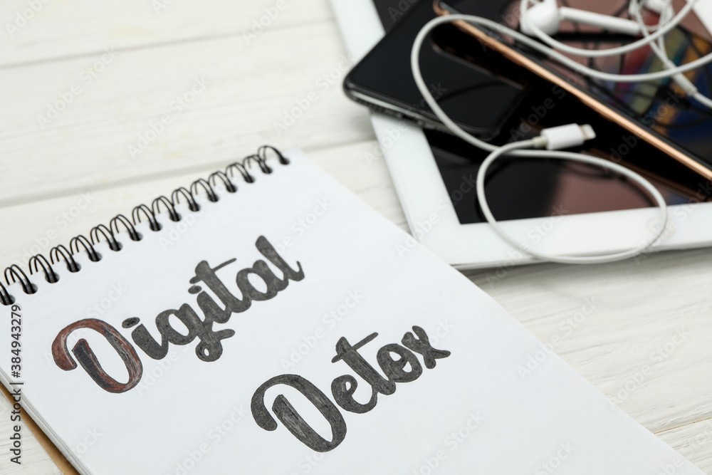 Notebook with phrase DIGITAL DETOX and different gadgets on white wooden table, closeup Notebook with phrase DIGITAL DETOX and different gadgets on white wooden table, closeup