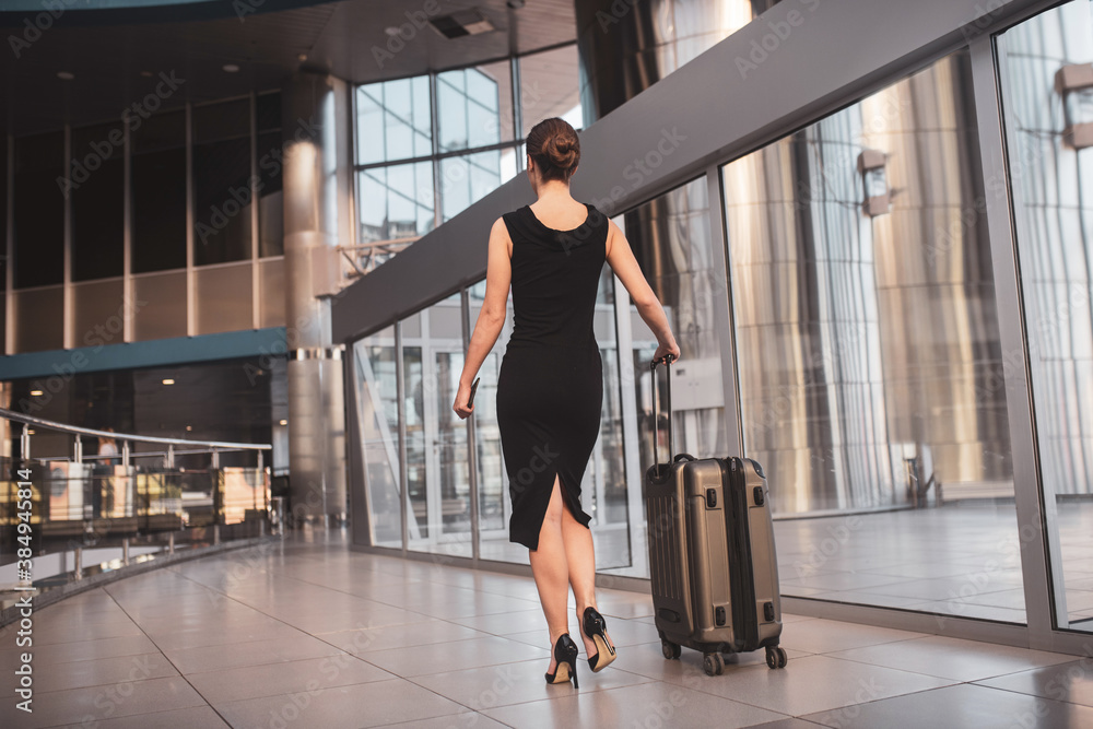 Obraz premium Elegant woman walking through the airport with a suitcase