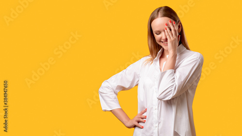 Shy woman. Fun joke. Positive attitude humor. Female lifestyle. Amused lady in white shirt smiling with facepalm gesture isolated on orange empty space commercial background. photo