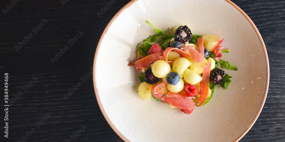 Salad of mixed summer berries. Seasonal summer salad with fruit and berries and Italian prosciutto meat.