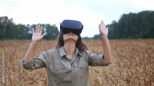 Beautiful girl in a golden wheat field uses virtual reality glasses