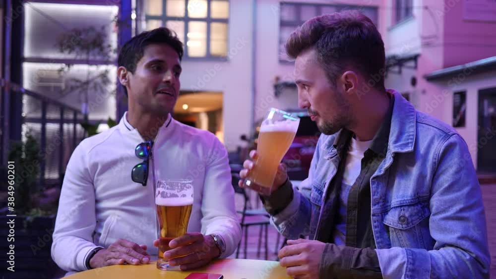 Hanging out two young guys friends in street bar drink alcohol beer from glass communicating in neon lights Hanging out two young guys friends in street bar drink alcohol beer from glass communicating in neon lights